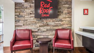 A Red Roof Inn reception area with a stone wall backdrop, two leather armchairs, and a small round table.