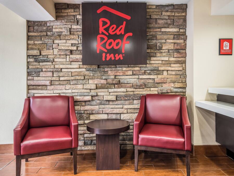 A Red Roof Inn reception area with a stone wall backdrop, two leather armchairs, and a small round table.