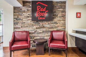 Zona de recepción de Red Roof Inn con un fondo de pared de piedra, dos sillones de cuero y una pequeña mesa redonda.