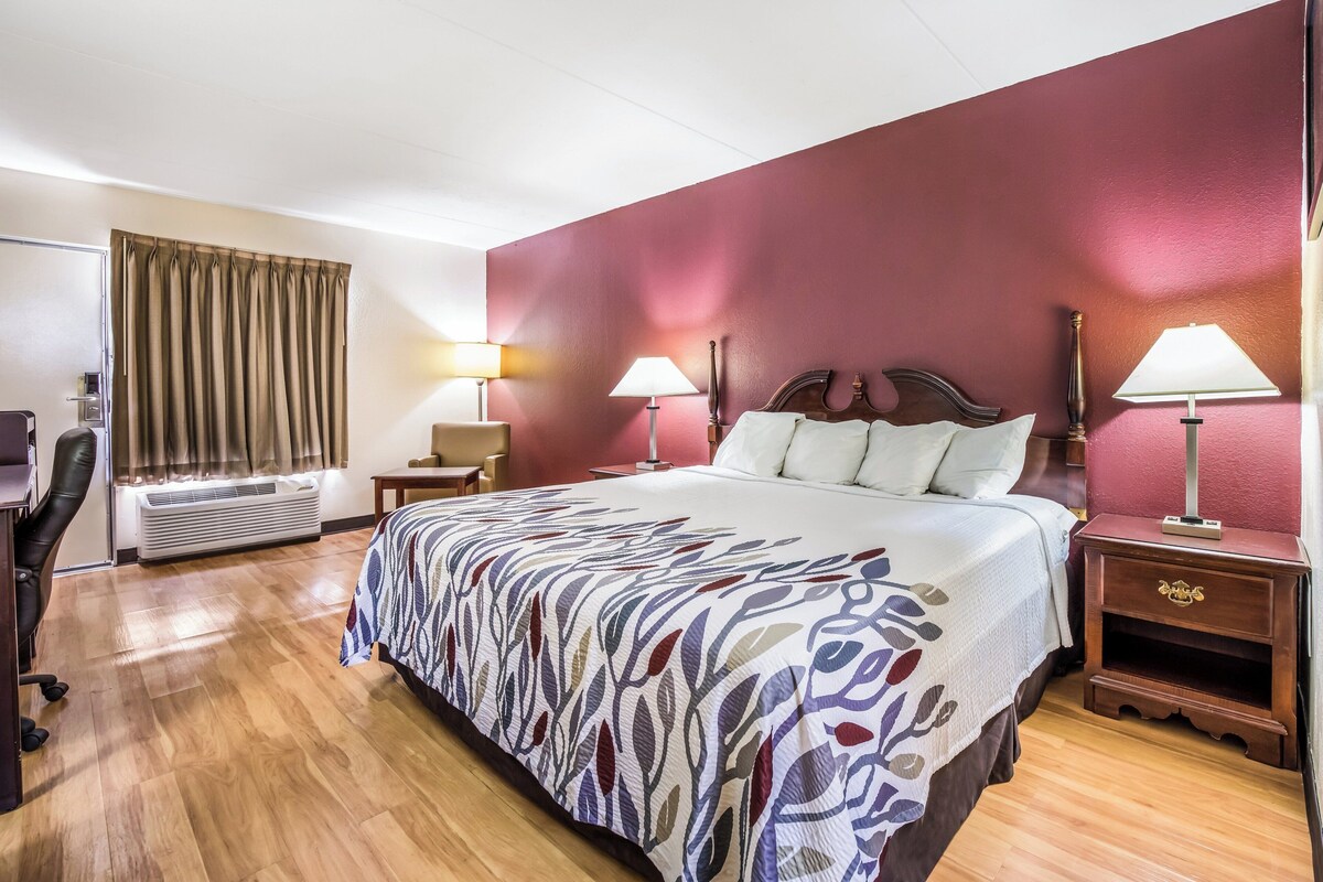 A hotel room with a large bed, two bedside lamps, a desk, and an air conditioning unit.