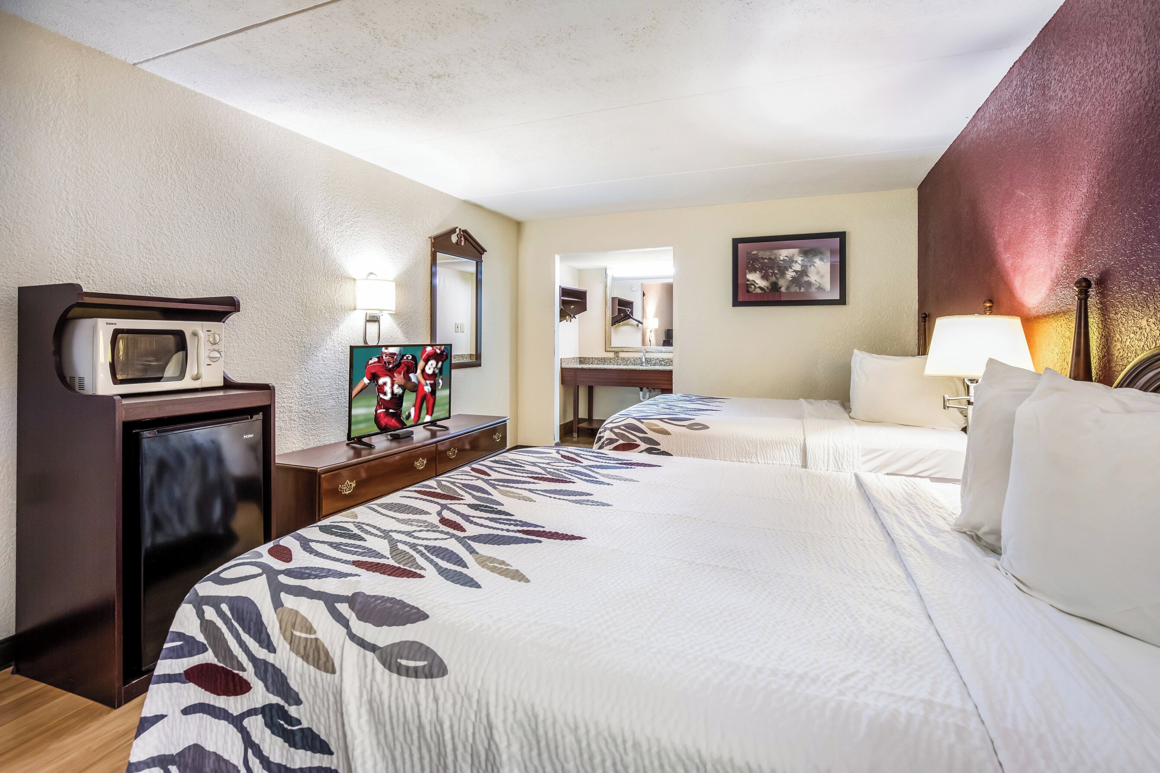 Une chambre d’hôtel comprenant un lit, un bureau avec un micro-ondes, une commode, un miroir et un tableau au mur.