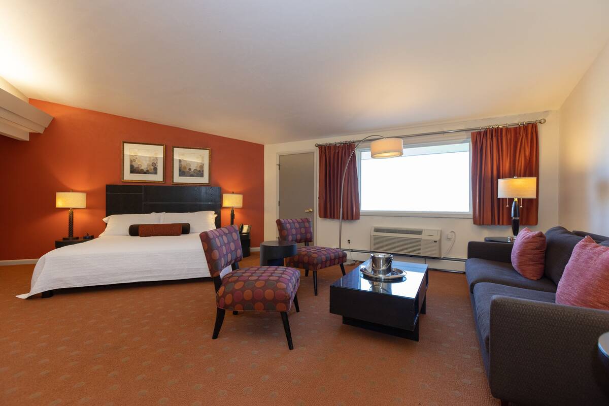 A hotel room with a bed, two armchairs, a sofa, a coffee table, and a desk.