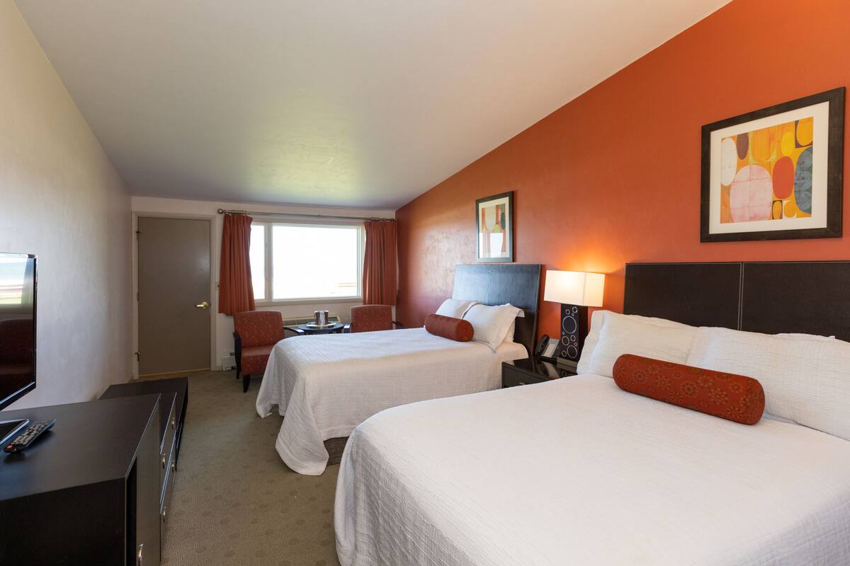 A hotel room with two beds, a desk, a chair, a TV, and a window with curtains.