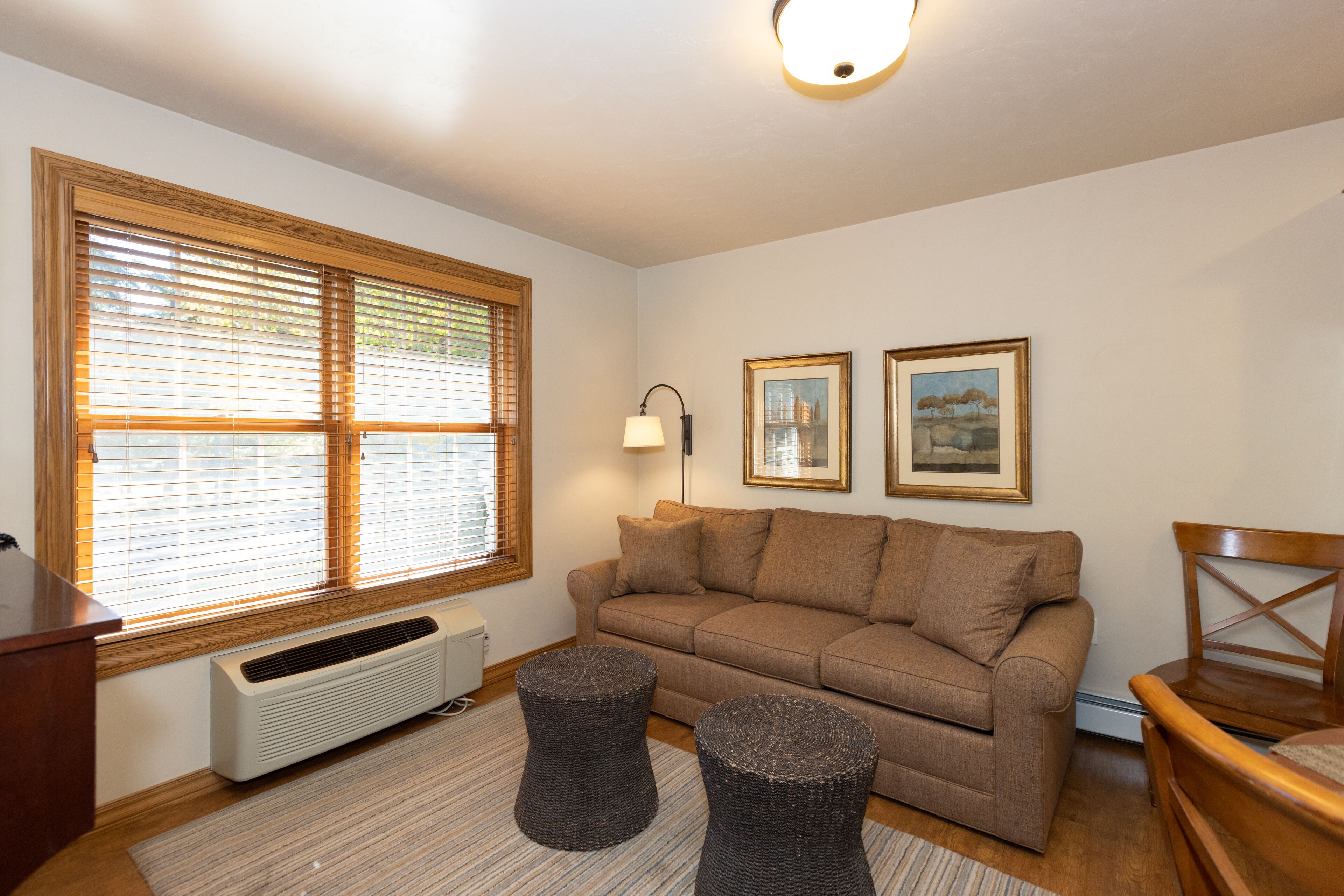 A living room with a beige sofa, two round wicker ottomans, a wooden desk, and a radiator.