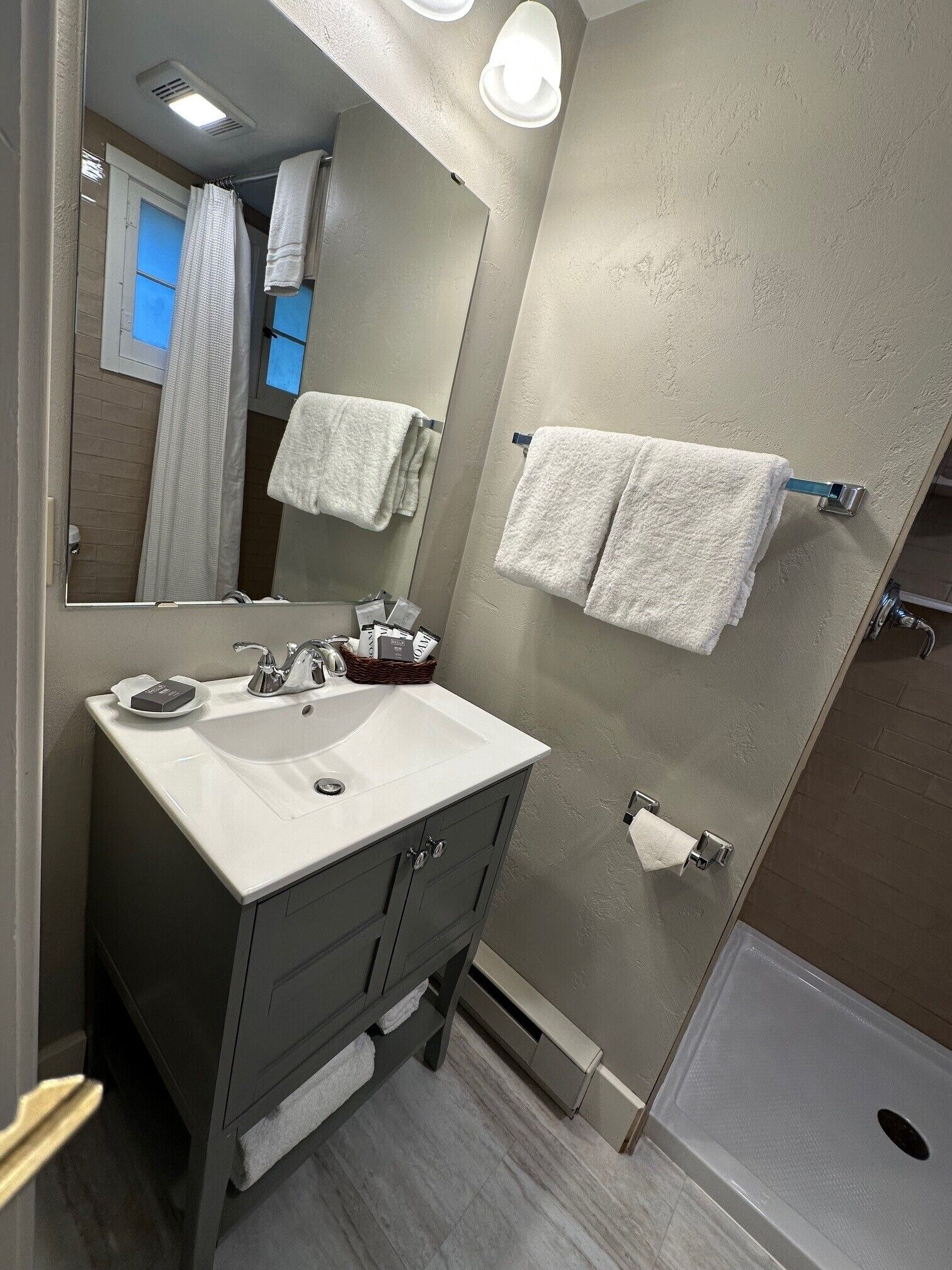 Un baño con lavamanos, espejo, toallero y ducha.