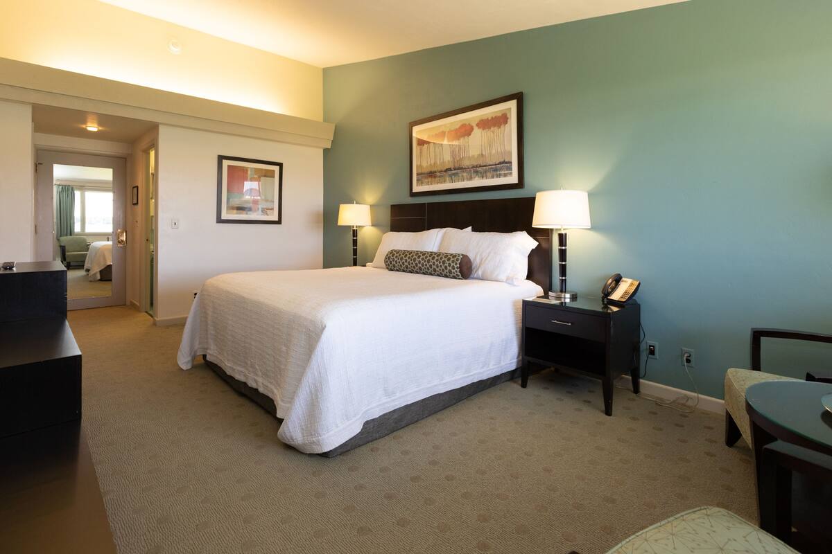 A hotel room with a large bed, two bedside tables with lamps, a desk, and a chair.