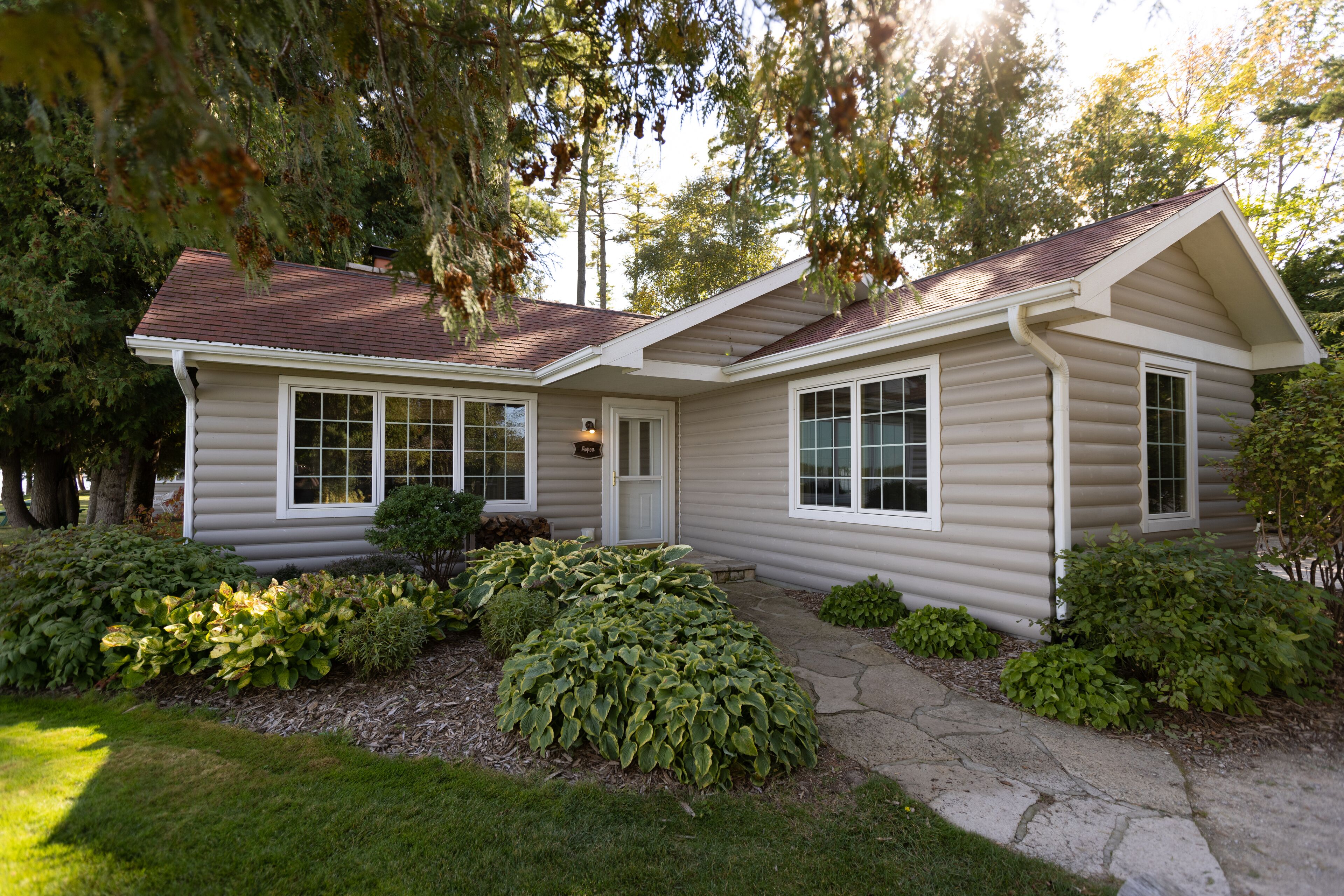 A single-story house with a gabled roof, a front porch, and a well-maintained garden with various shrubs and a lawn.