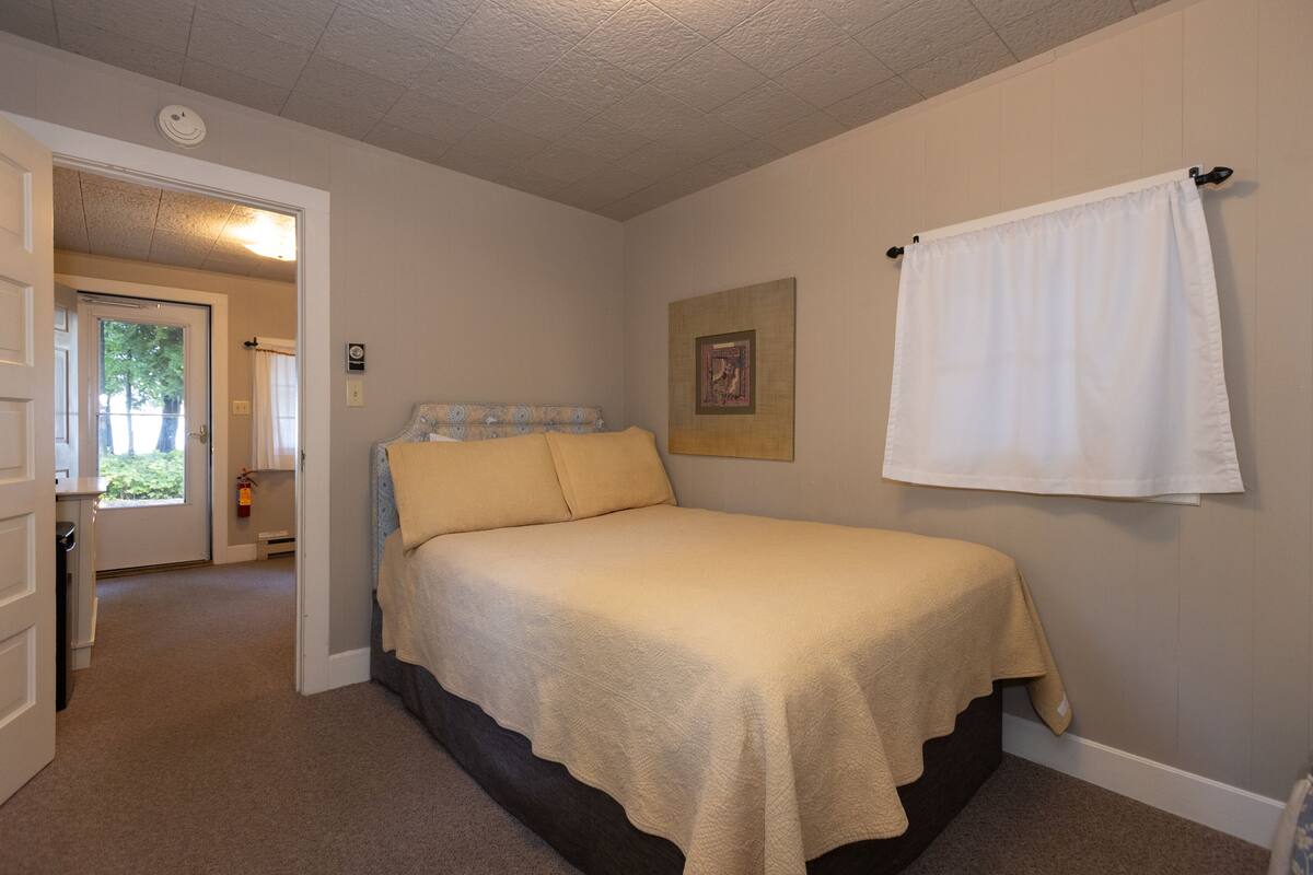A bedroom with a bed, a door, a window, and a wall-mounted towel.
