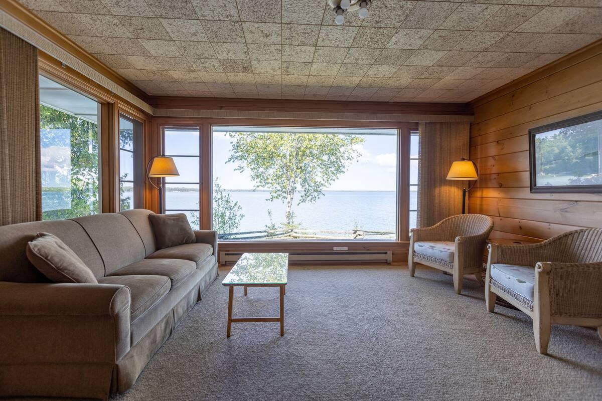A cozy room with a large window, a sofa, two chairs, a small table, and two lamps.
