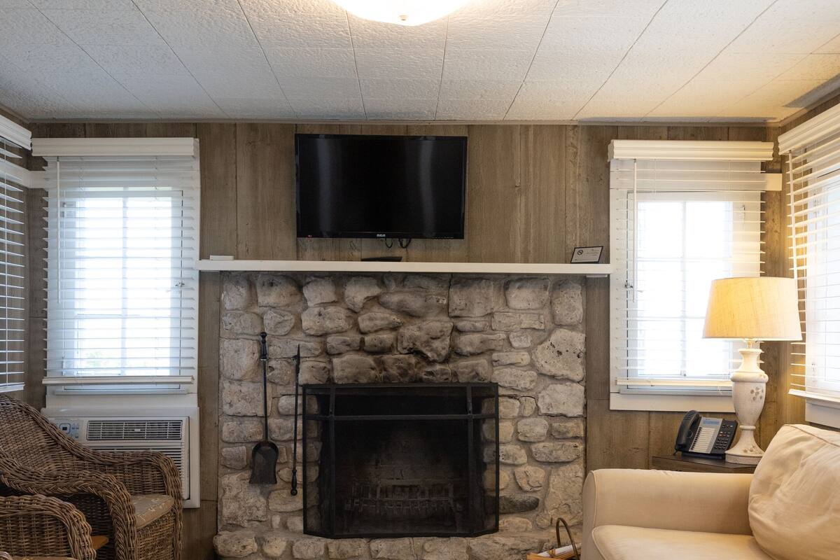 A living room with a stone fireplace, wicker furniture, a beige sofa, and a mounted TV.