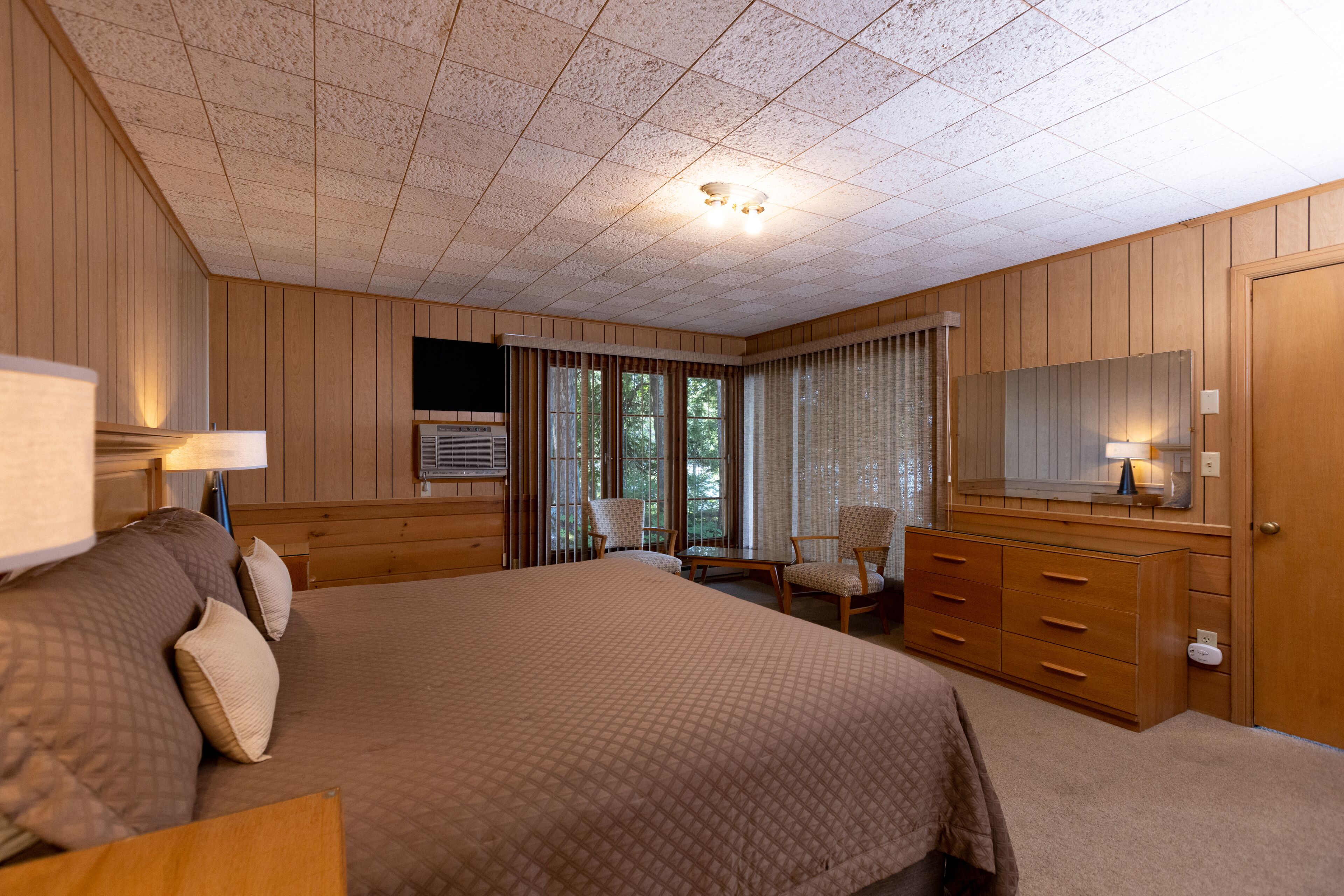 Une chambre d’hôtel avec un grand lit, des boiseries, une télévision, un bureau avec une lampe et une commode.