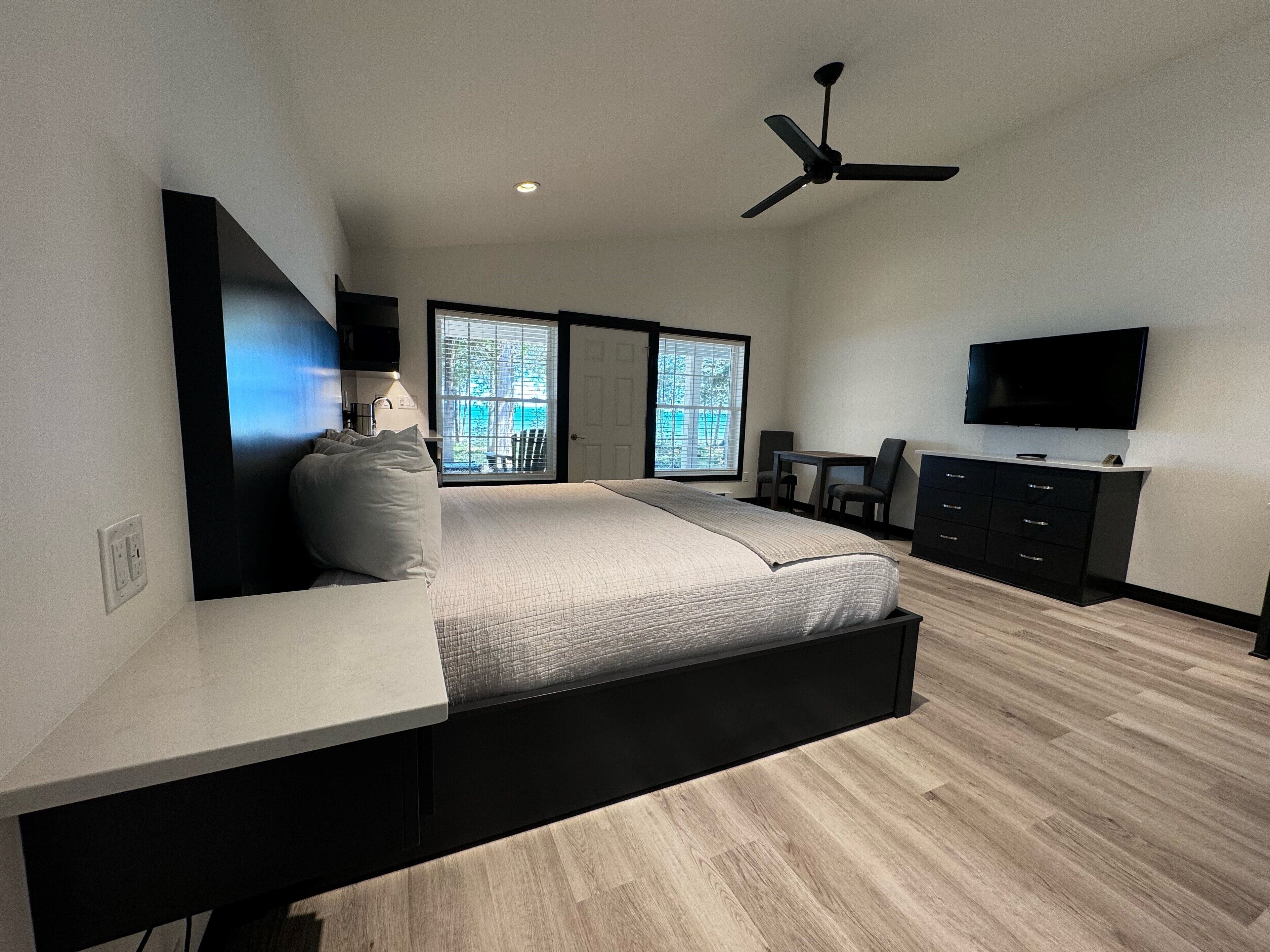 Une chambre moderne équipée d’un lit, d’un bureau, d’une chaise, d’une télévision et d’un ventilateur de plafond.