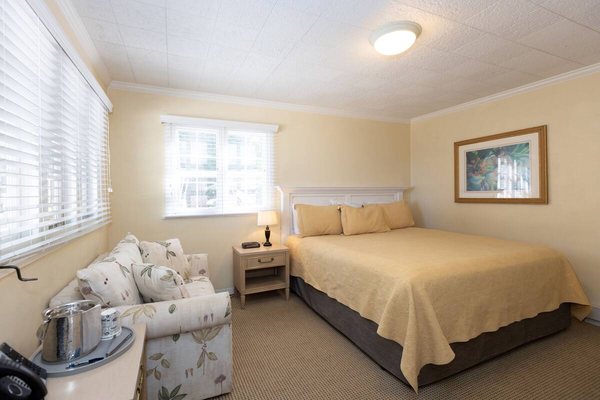 A neatly arranged bedroom with a bed, bedside table, lamp, and a small seating area with a chair.