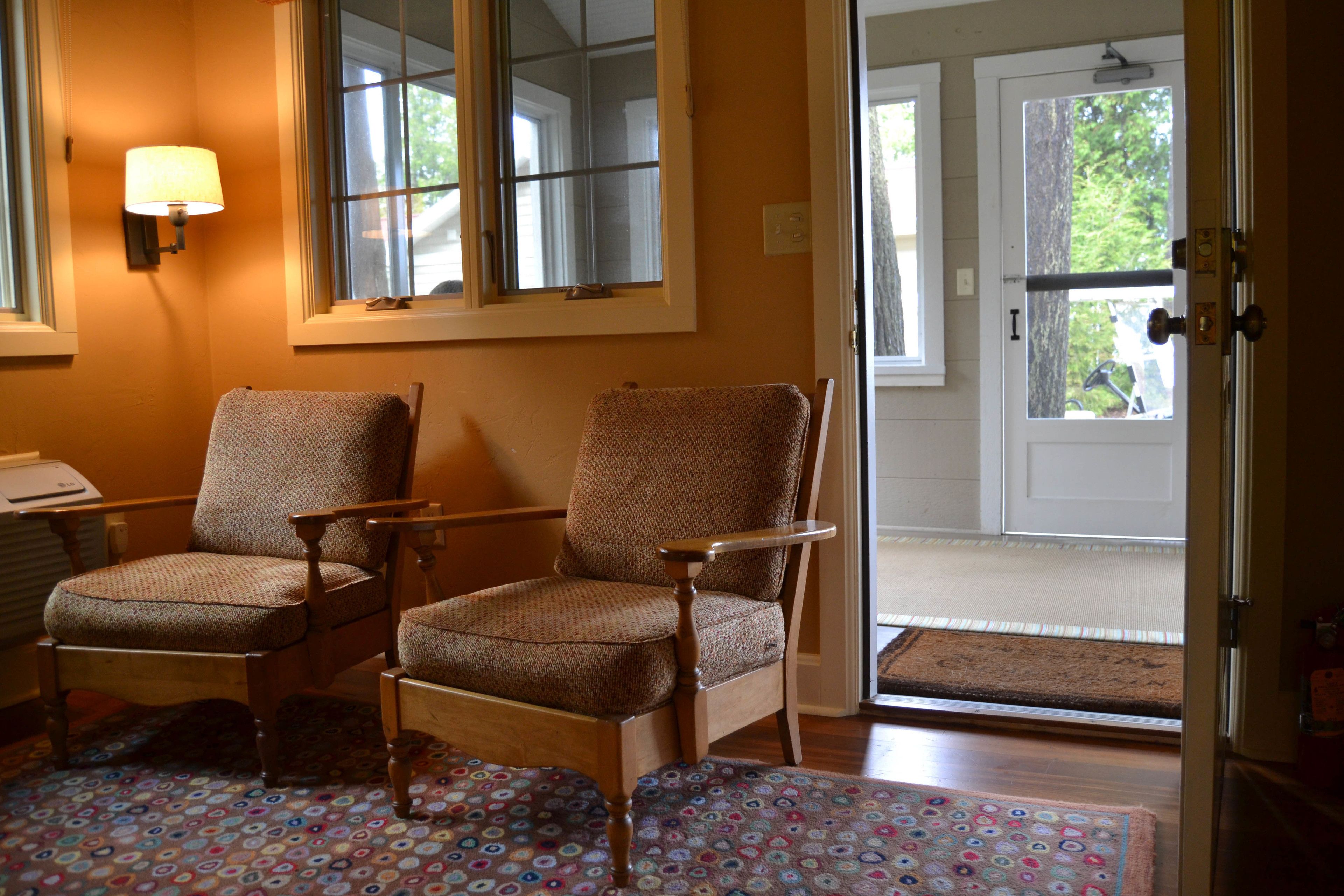 Une pièce avec deux chaises en bois, une lampe, une fenêtre et une porte donnant sur l’extérieur.