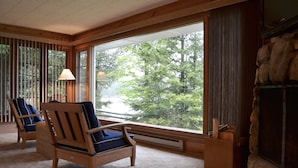 A cozy room with large windows, a fireplace, and two wooden chairs with cushions. - Gordon Lodge (Baileys Harbor)