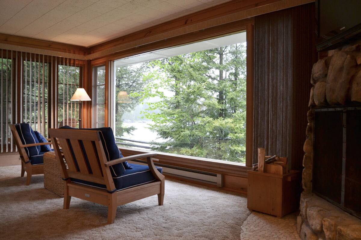 A cozy room with large windows, a fireplace, and two wooden chairs with cushions.