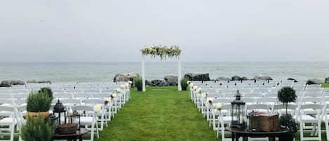A beachside wedding setup with white chairs and a floral arch.