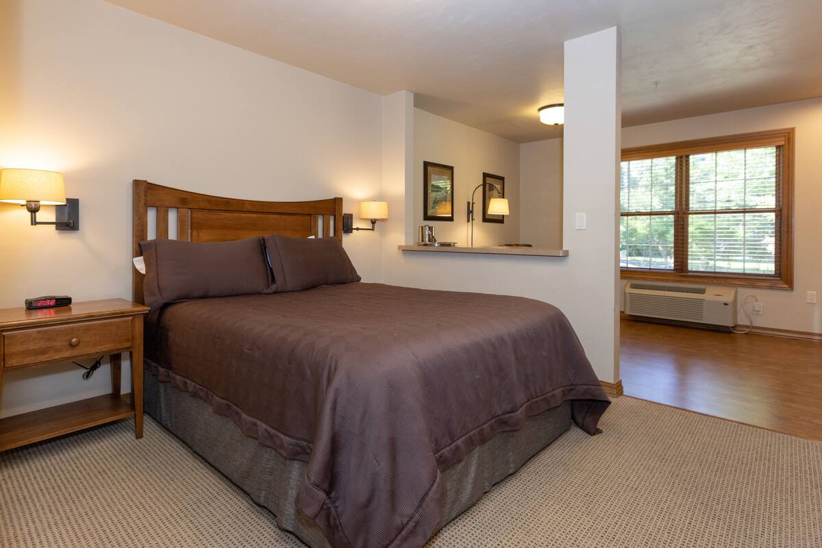 A neatly arranged bedroom with a bed, bedside lamps, a nightstand, and a window with blinds.