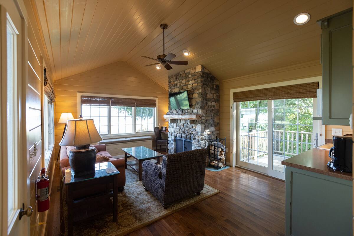 A cozy living room with a stone fireplace, wooden ceiling, and a comfortable seating area.