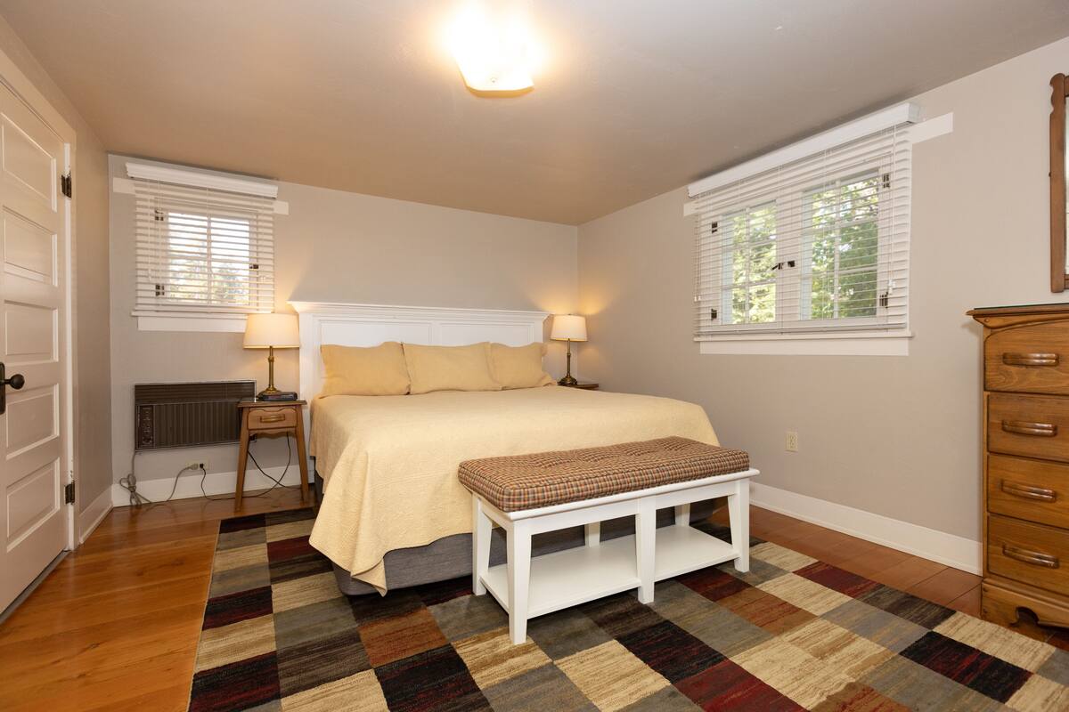 A bedroom with a bed, bedside lamps, a bench, a dresser, and a radiator.