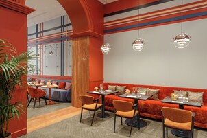 Un ristorante con una parete a righe rosse e blu, sedute arancioni e lampade a sospensione.