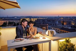 Un couple est assis à une table, devant une vue sur la ville, avec une lampe et une petite plante sur la table.