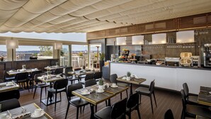 A restaurant with tables and chairs, a counter with food and drinks, and a view of the city. - The Independent Hotel (Rome)