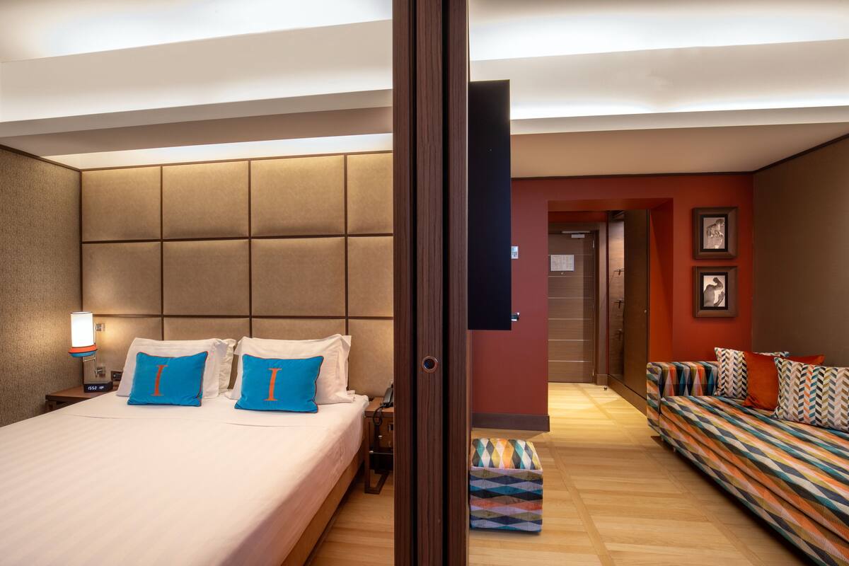 A hotel room with a bed, a sofa, a nightstand, and a wall-mounted TV.