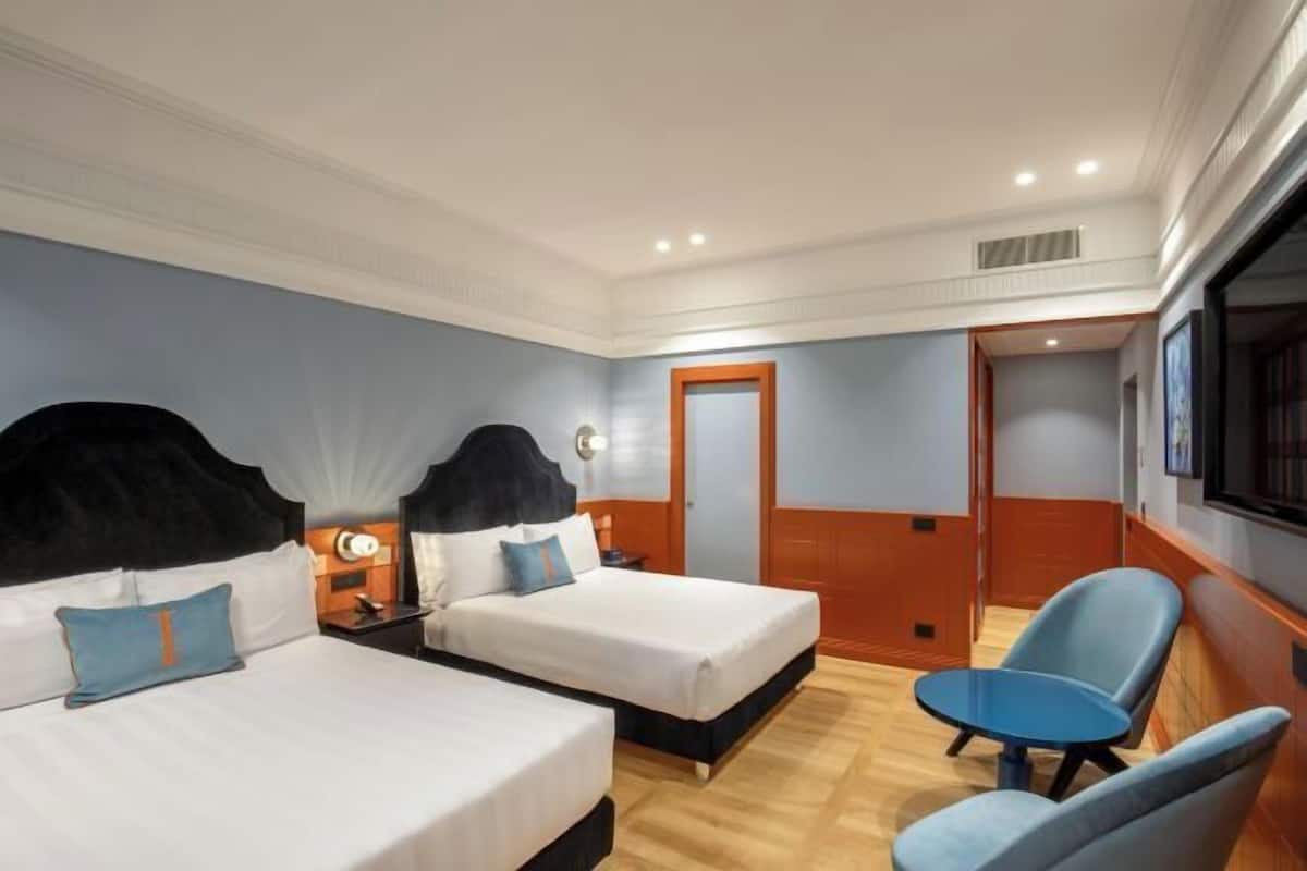 A hotel room with two beds, a desk, a chair, and a TV.
