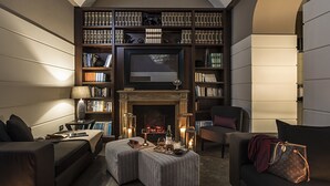 A cozy living room with a fireplace, bookshelves, a television, and comfortable seating. - The Independent Hotel (Rome)