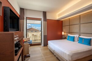 Una camera d'albergo con un letto, una televisione, una scrivania con una sedia e un balcone affacciato su edifici.