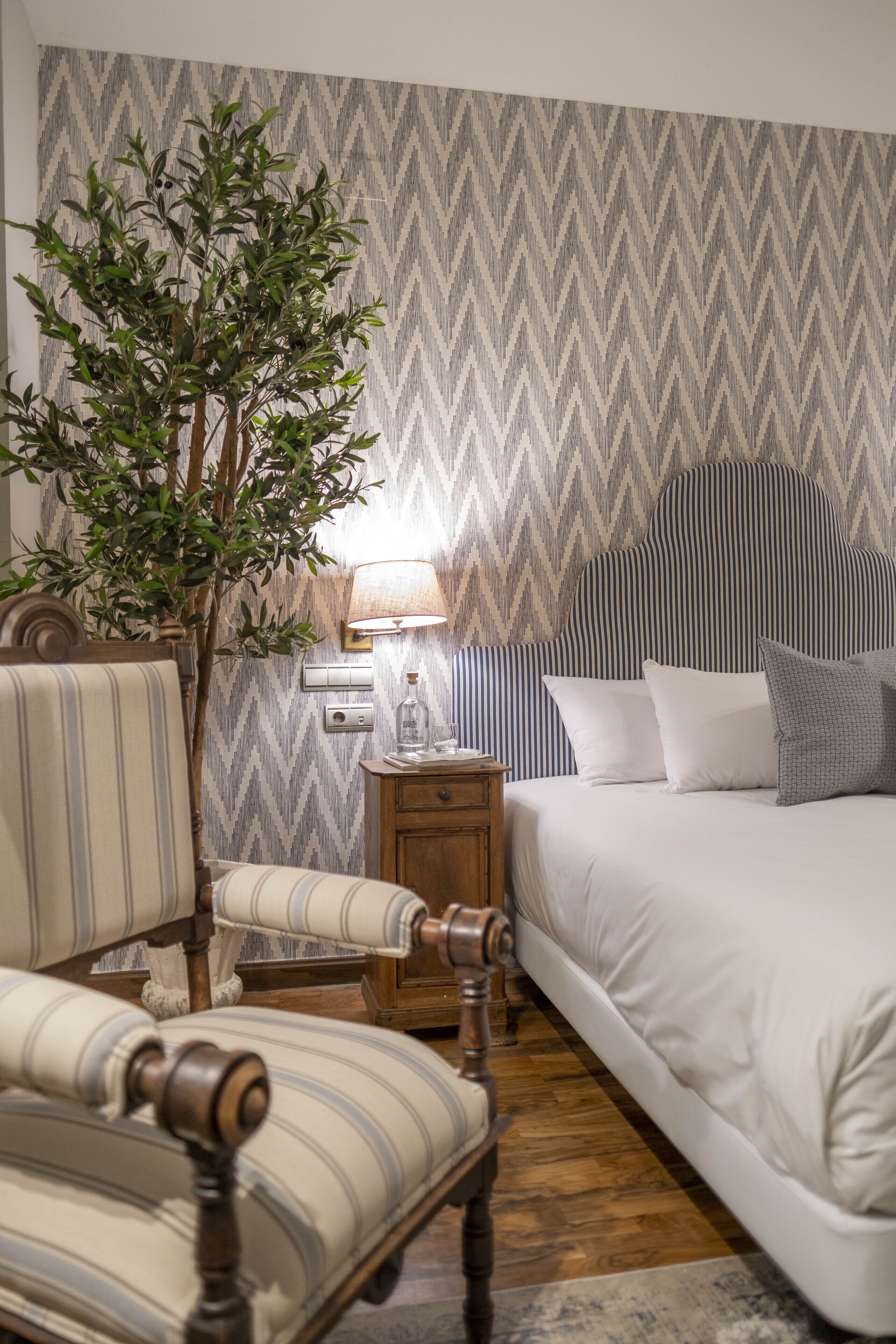 Ein Hotelzimmer mit einem Bett, einem Sessel, einem Nachttisch, einer Lampe und einer Topfpflanze.