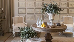 A room with a high ceiling featuring intricate woodwork and a series of framed architectural drawings on the wall.