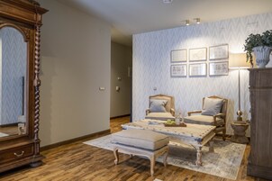 Um quarto com piso de madeira, dois poltronas, uma mesa de centro, um espelho e uma parede com quadros.
