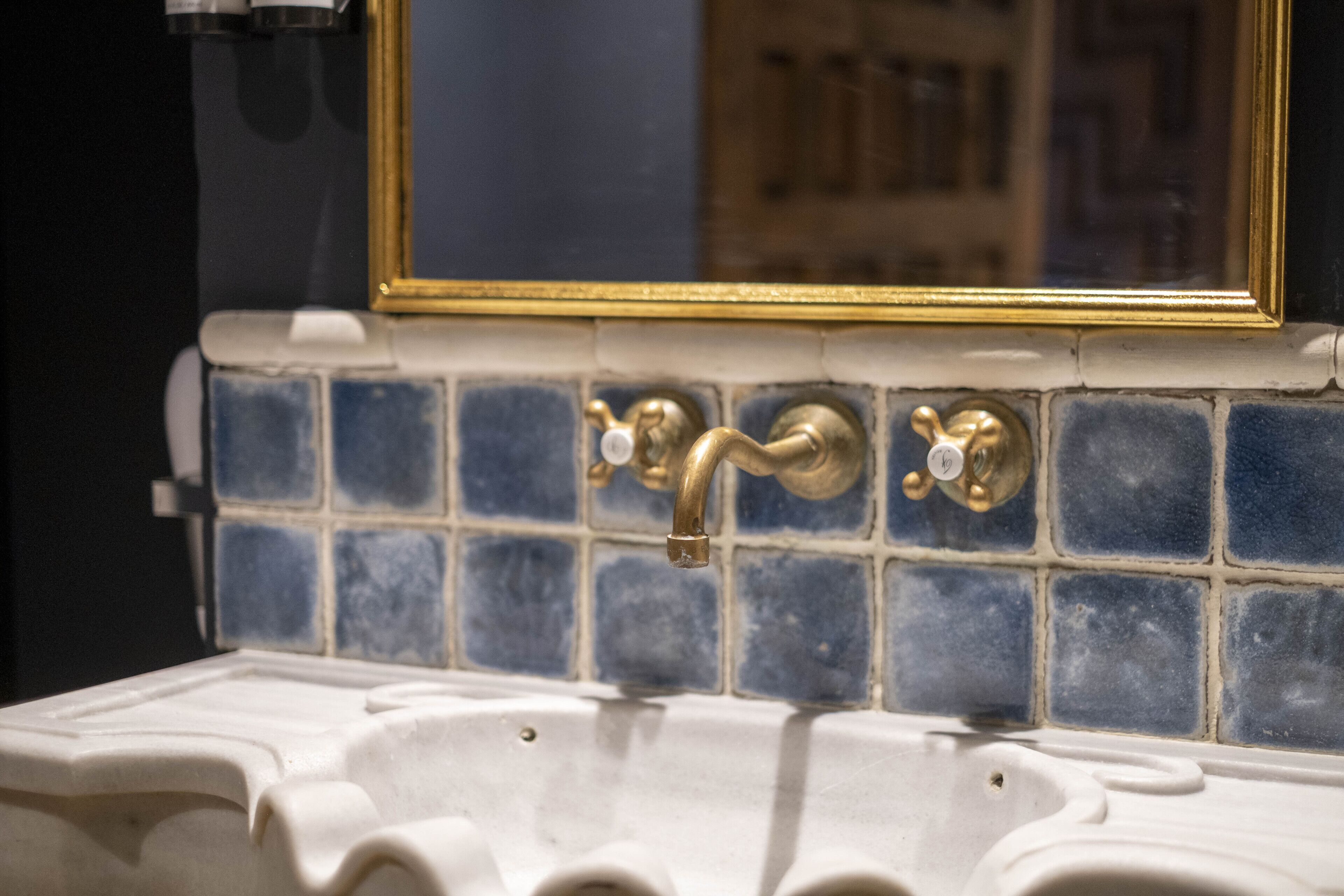 A bathroom with a white sink, blue-tiled backsplash, and a gold-framed mirror.