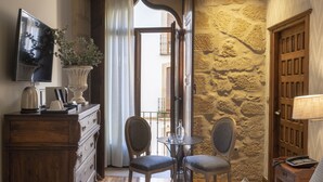 A hotel room with a bed, a dresser, a television, a table with two chairs, and a stone wall.
