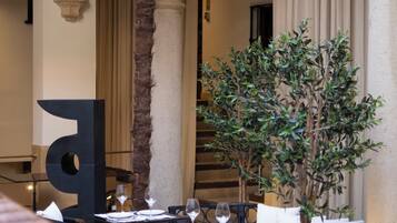 A dining area with tables and chairs, a palm tree, and a large decorative letter 'A'.