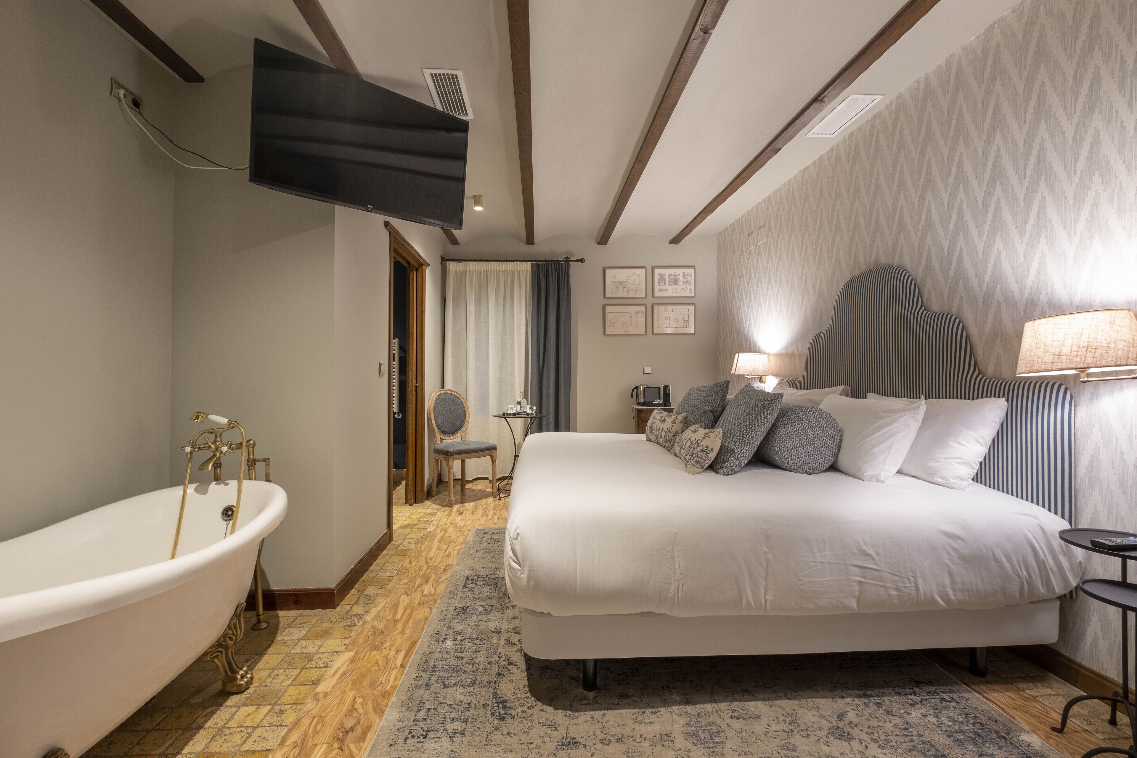 A modern hotel room with a large bed, a bathtub, a television, and a desk with a chair.