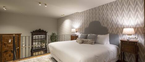 A bedroom with a large bed, two bedside tables with lamps, a wooden wardrobe, and a patterned wallpaper.
