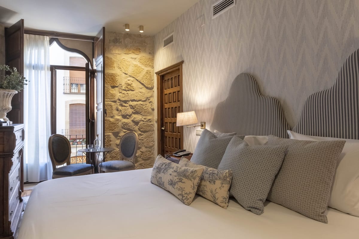 A hotel room with a large bed, a stone wall, a wooden door, and a view of the outside balcony.