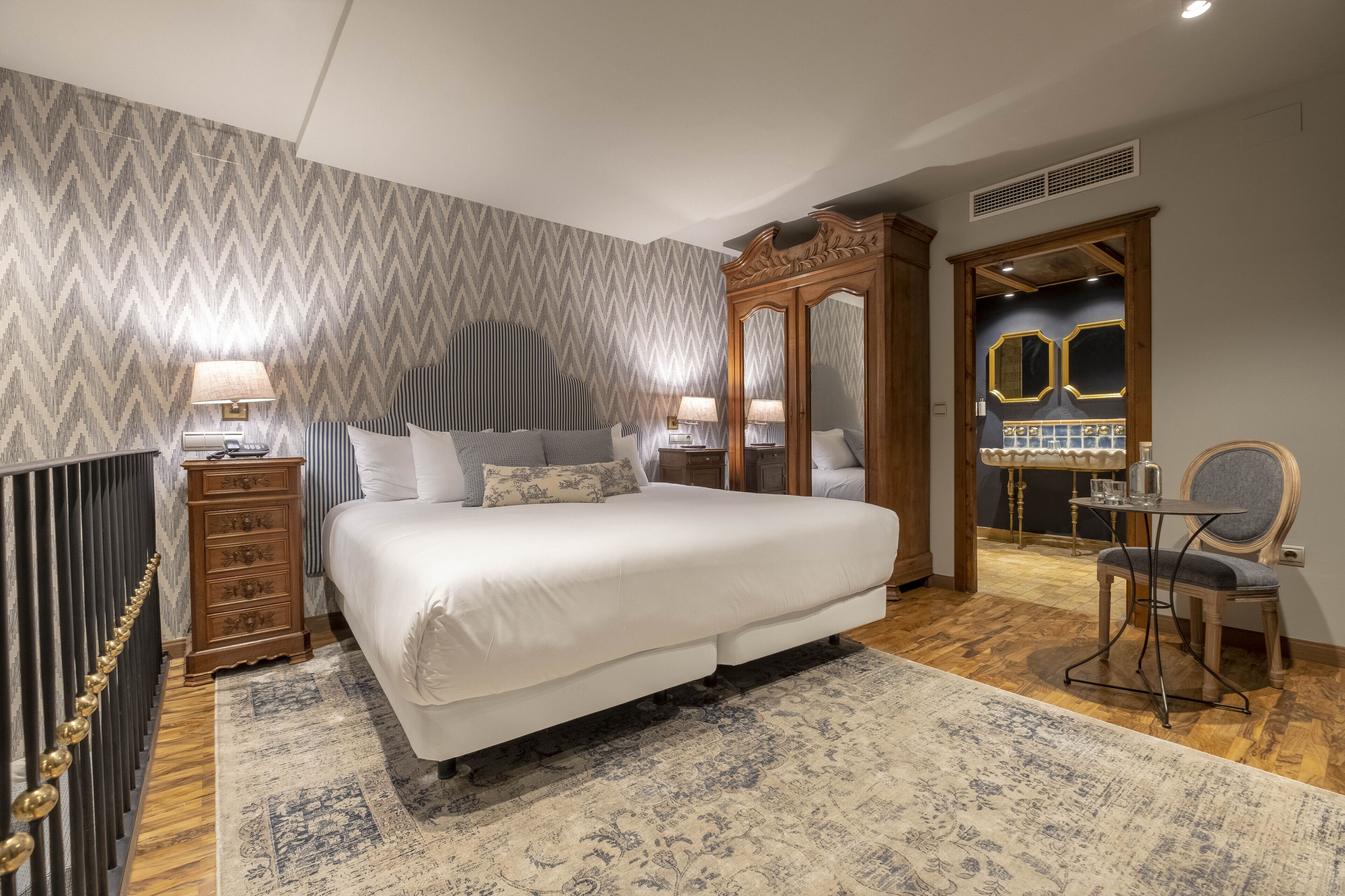 Un dormitorio amplio con una cama grande, un aparador de madera, una silla y un espejo.