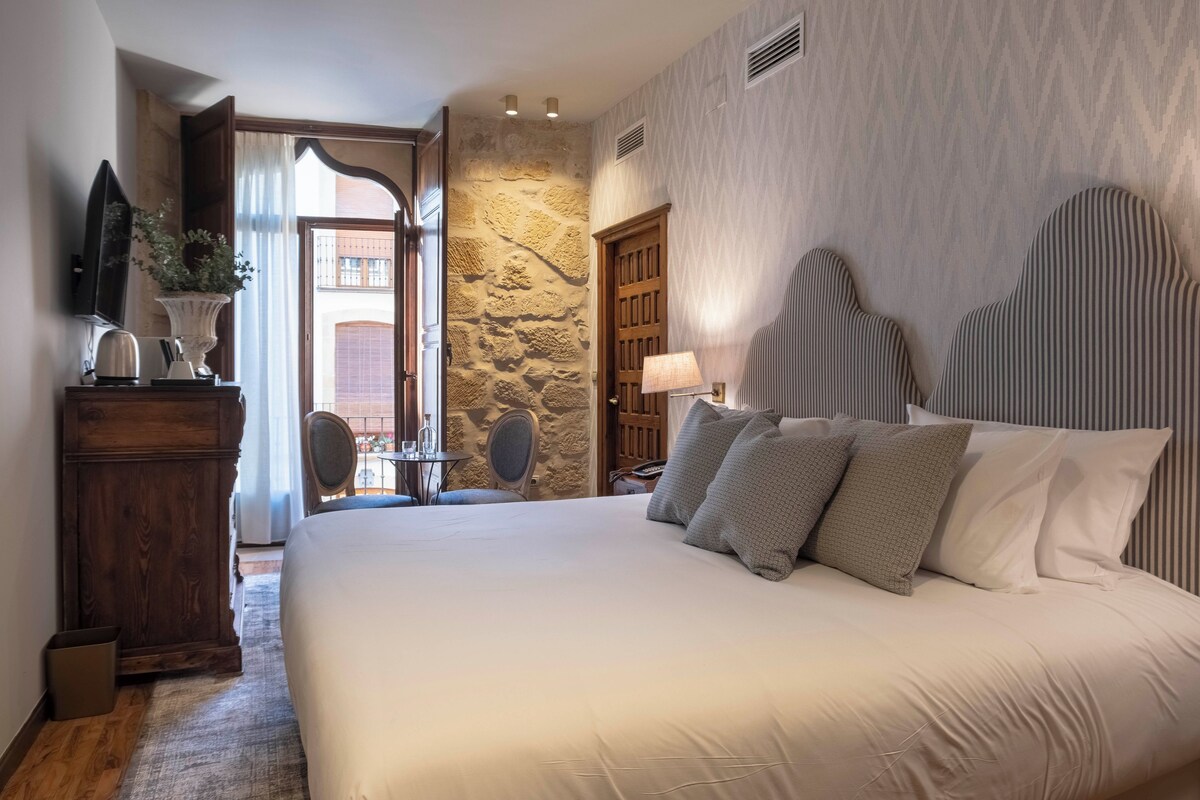 A bedroom with a large bed, a wooden dresser, a mirror, and a stone wall.