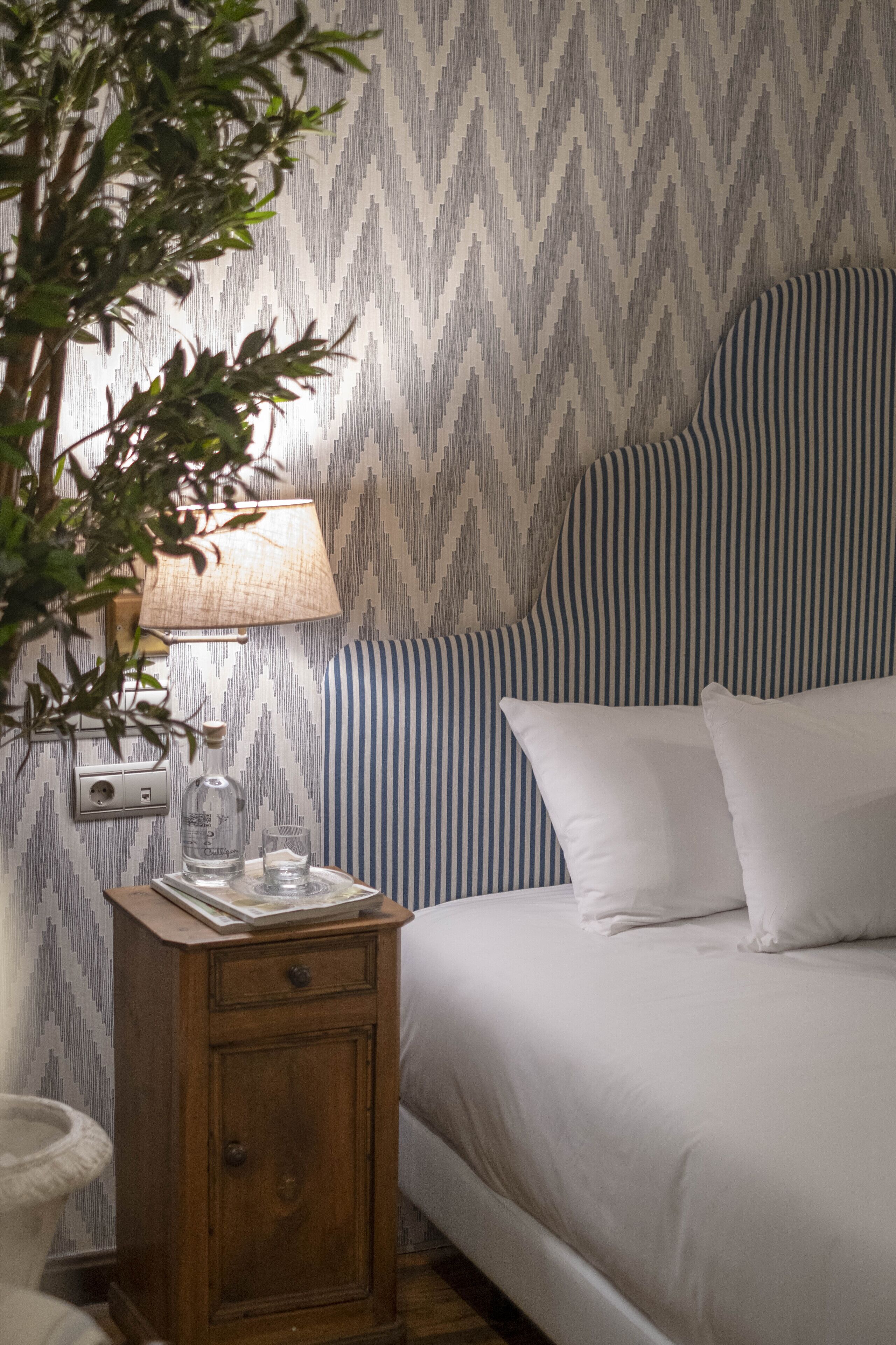 A neatly made bed with white linens, a striped headboard, and a bedside table with a lamp, glass, and a book.