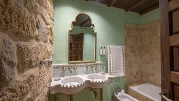 Une salle de bain avec un mur en pierre, une porte en bois, un miroir doté d’un cadre orné et une baignoire.