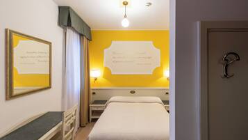 A hotel room with a bed, a desk, and a chair. There are two wall-mounted lamps and a framed quote on the wall.