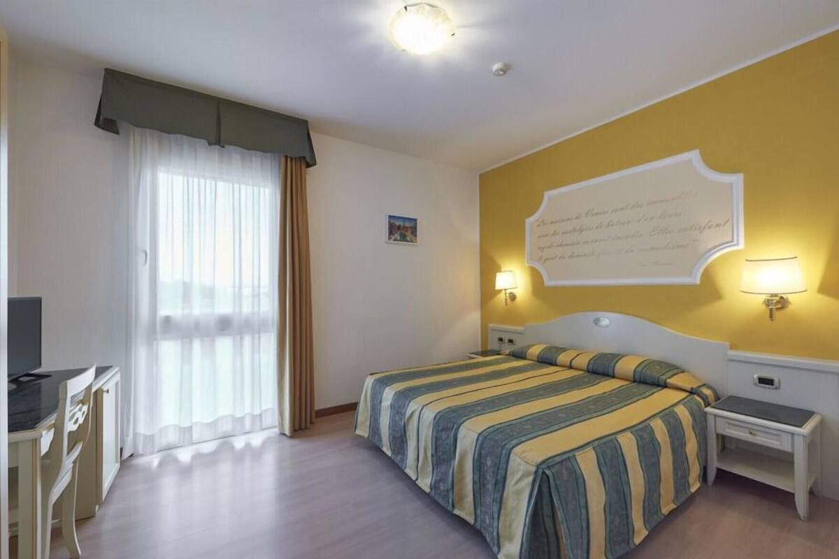 A hotel room with a bed, bedside tables, a desk, and a television.