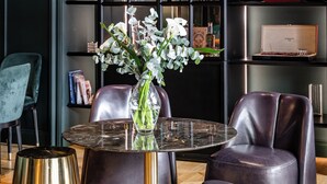 A modern interior with a round table, leather chairs, a glass vase with flowers, and a black shelving unit with various items.
