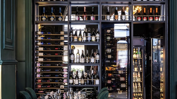 A bar area with a long counter, multiple shelves of bottles, and plush green chairs.