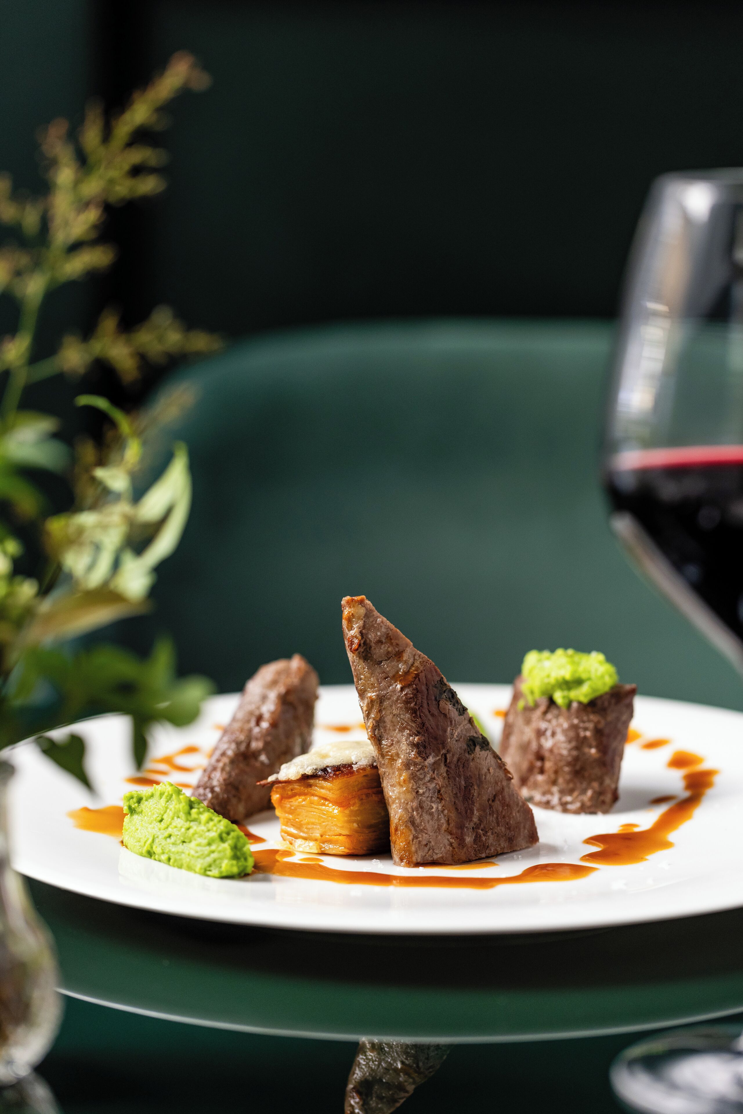 A plate of food with a green sauce and a glass of red wine.