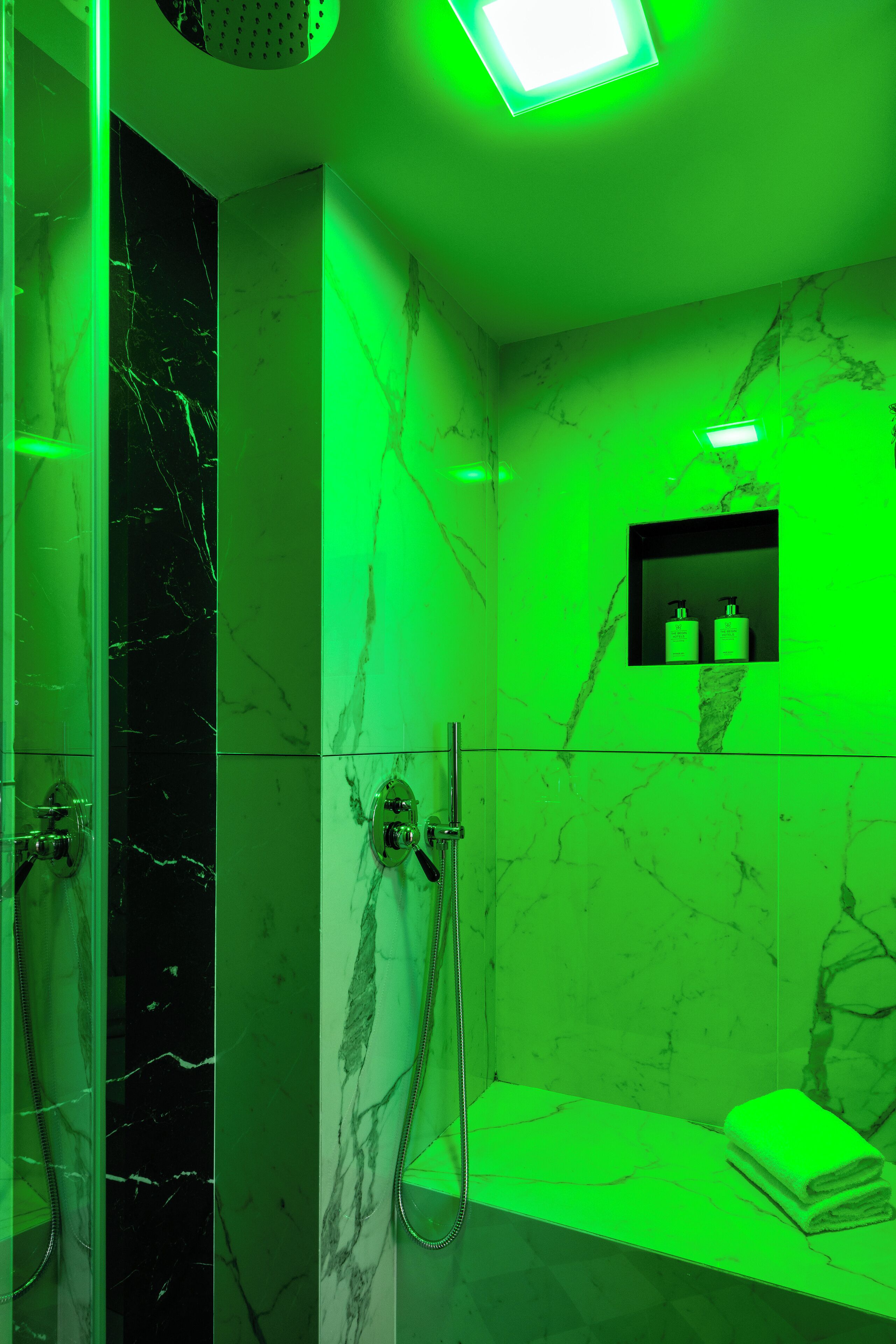 A bathroom with a glass shower enclosure, marble walls, and a green-lit vanity area.